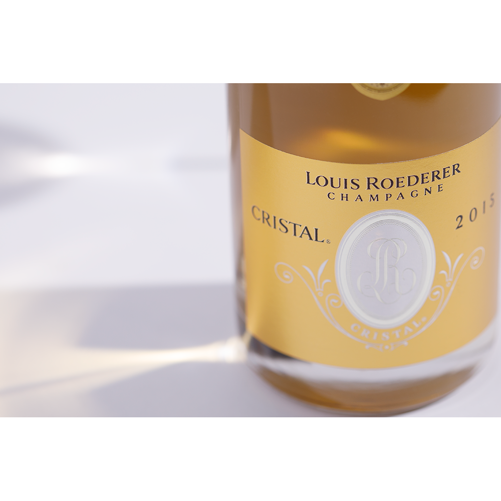 Close up label on a bottle of Louis Roederer Cristal 2015 on a white table with shadows of the bottle and 2 champagne glasses