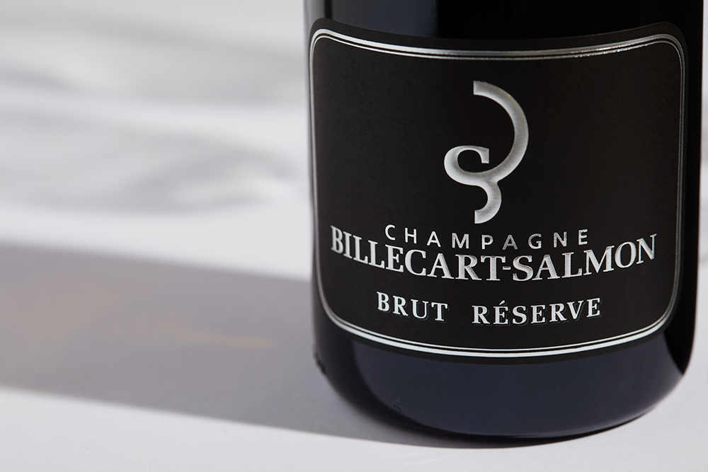 Close up label on a bottle of Billecart-Salmon Brut Réserve on a white table with shadows of the bottle and 2 champagne glasses