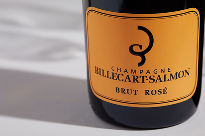 Close up label on a bottle of Billecart-Salmon Brut Rosé on a white table with shadows of the bottle and 2 champagne glasses