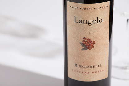 Close up label on a bottle of Bucciarelli Langelo Rosso IGT Toscana 2019 Castellina on a white table with shadows of the bottle and 2 wine glasses