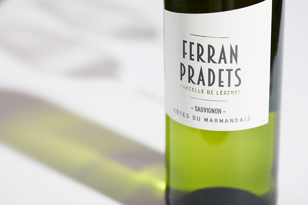 Close up label on a bottle of Caves du Marmandais Ferran Pradets Sauvignon Blanc 2022 Cotes du Marmandais on a white table with shadows of the bottle and 2 wine glasses