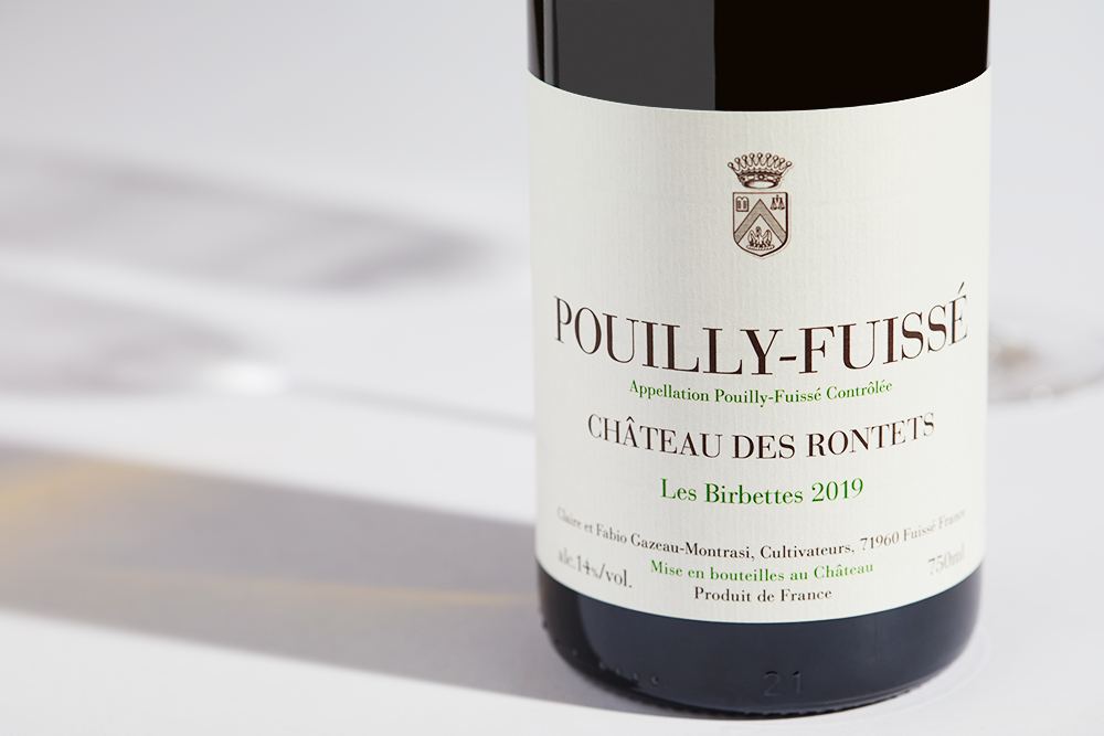 Close up label on a bottle of Chateau des Rontets Pouilly Fuisse Birbettes 2019 on a white table with shadows of the bottle and 2 wine glasses