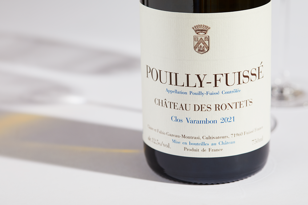 Close up label on a bottle of Chateau des Rontets Pouilly Fuisse Clos Varambon 2021 on a white table with shadows of the bottle and 2 wine glasses