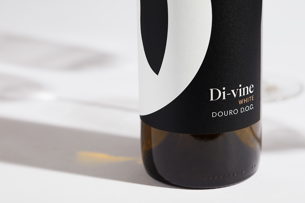 Close up label on a bottle of Di-vine white wine on a white table with shadows of the bottle and 2 wine glasses