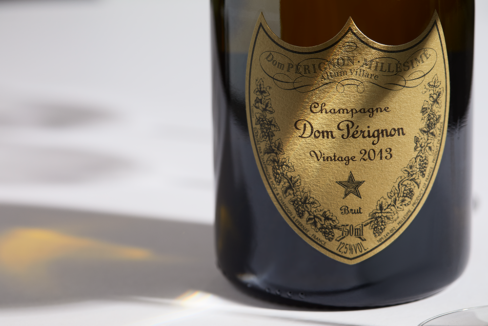 Close up label on a bottle of Dom Pérignon Brut 2013 on a white table with shadows of the bottle and 2 champagne glasses