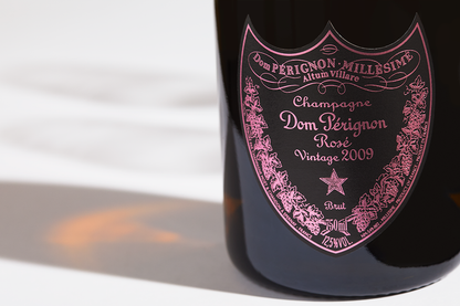 Close up label on a bottle of Dom Perignon Rosé 2009 on a white table with shadows of the bottle and 2 champagne glasses