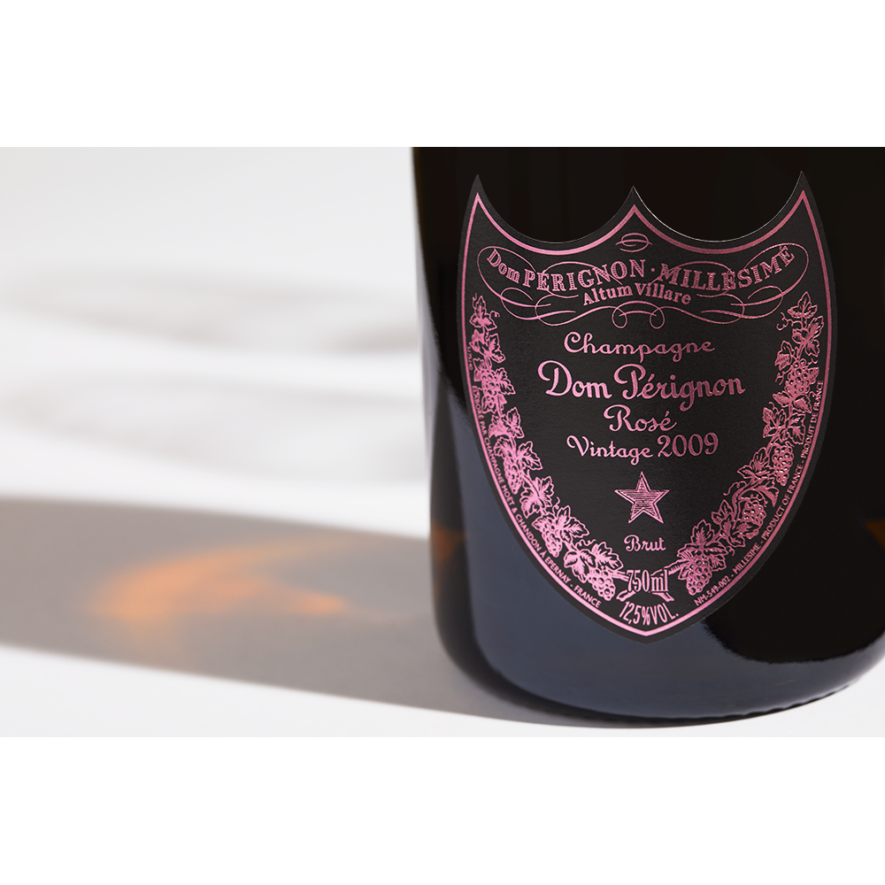 Close up label on a bottle of Dom Perignon Rosé 2009 on a white table with shadows of the bottle and 2 champagne glasses