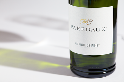 Close up label on a bottle of Domaine des Lauriers Paredaux Picpoul de Pinet 2022 on a white table with shadows of the bottle and 2 wine glasses