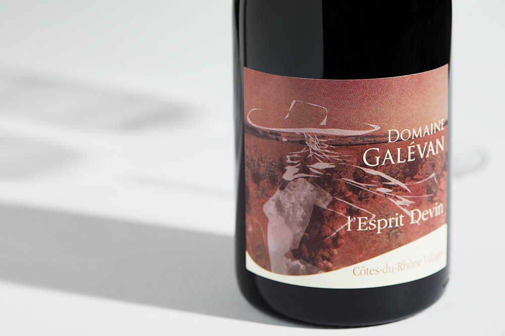 Close up label on a bottle of Galevan L Esprit Devin Cotes du Rhone Villages 2020 on a white table with shadows of the bottle and 2 wine glasses