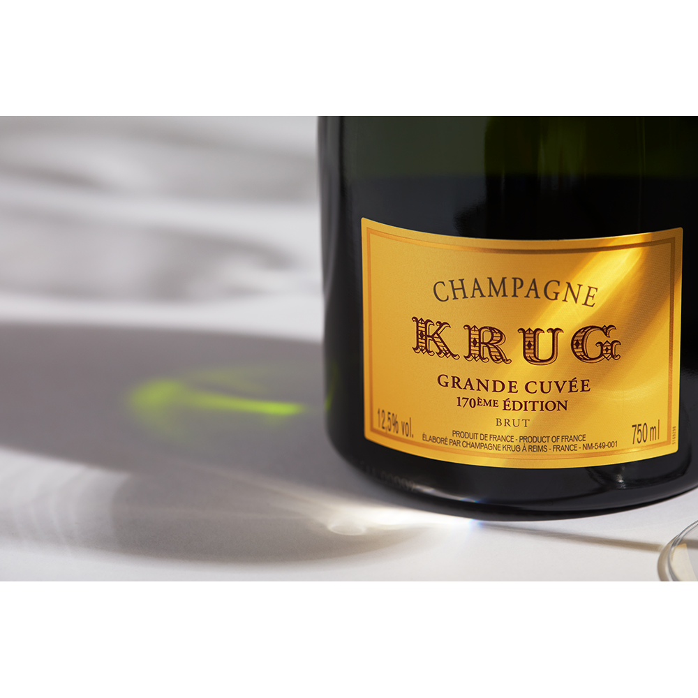 Close up label on a bottle of Krug Grand Cuvée 170th Edition on a white table with shadows of the bottle and 2 champagne glasses