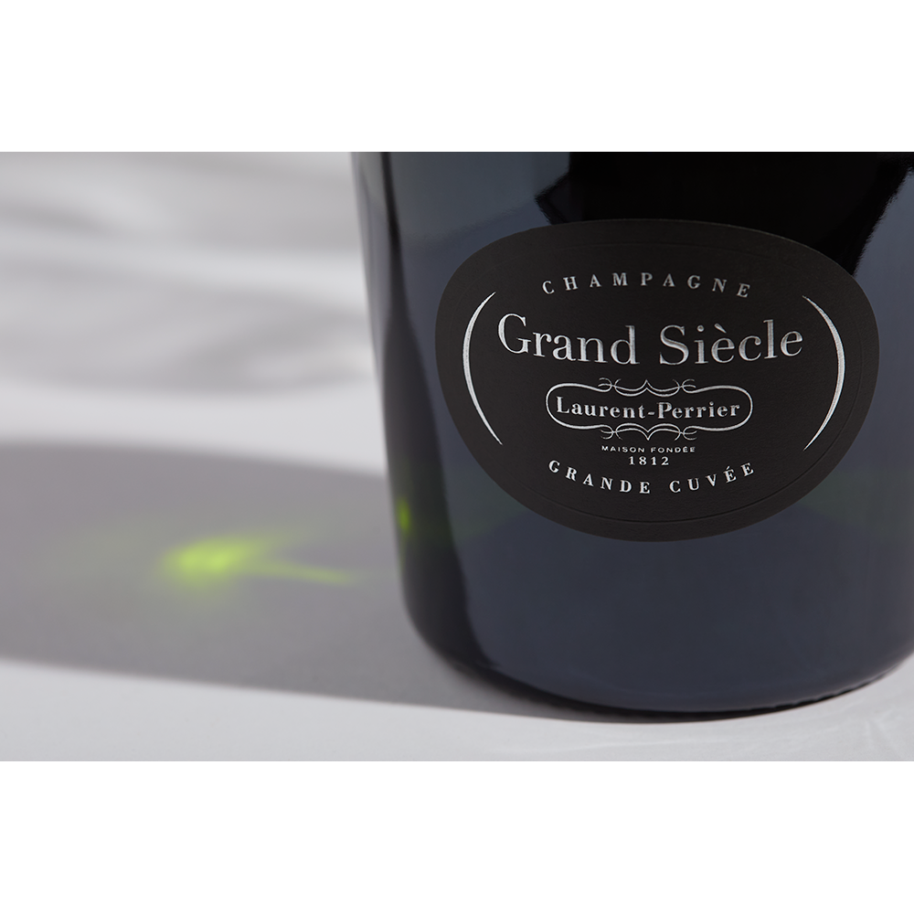 Close up label on a bottle of Laurent-Perrier Grand Siècle No. 26 on a white table with shadows of the bottle and 2 champagne glasses