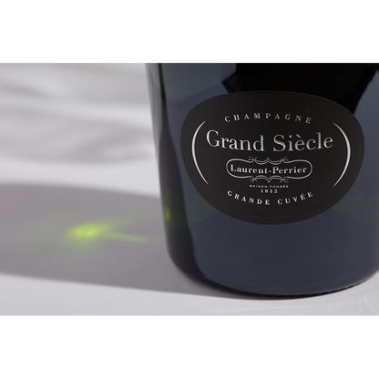 Close up label on a bottle of Laurent-Perrier Grand Siècle No. 26 on a white table with shadows of the bottle and 2 champagne glasses