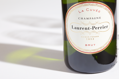 Close up label on a bottle of Laurent-Perrier La Cuvée Brut on a white table with shadows of the bottle and 2 champagne glasses