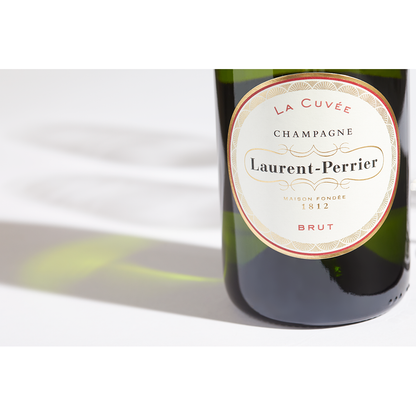 Close up label on a bottle of Laurent-Perrier La Cuvée Brut on a white table with shadows of the bottle and 2 champagne glasses