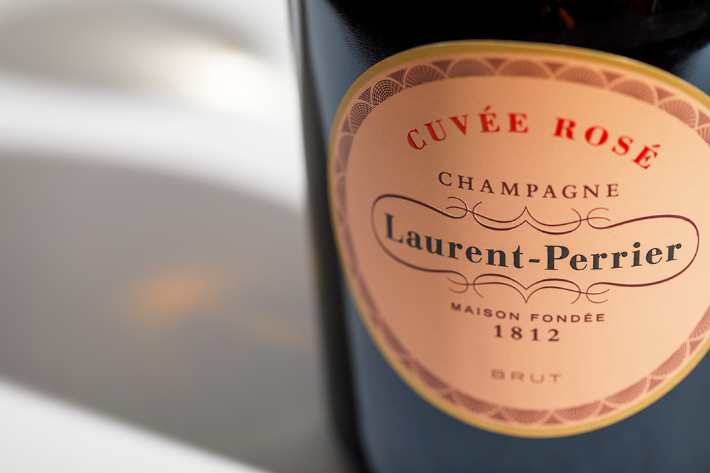 Close up label on a bottle of Laurent-Perrier Rosé on a white table with shadows of the bottle and 2 champagne glasses