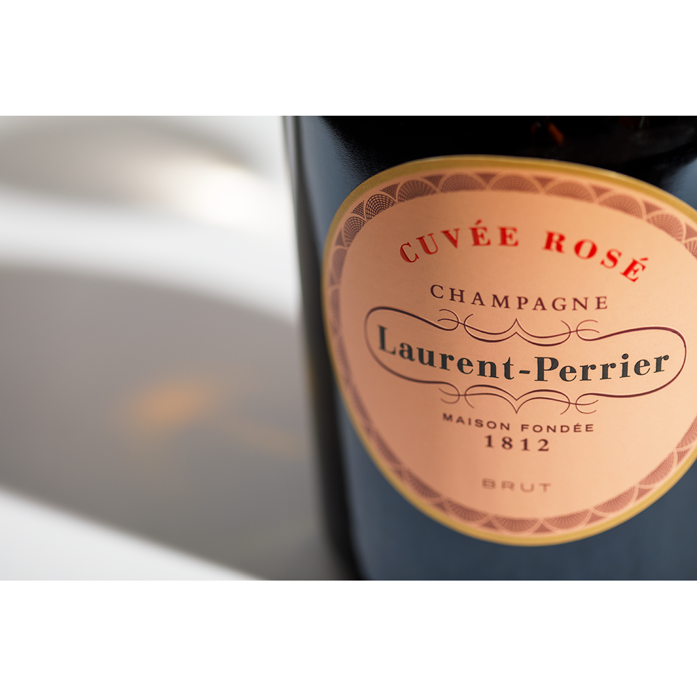 Close up label on a bottle of Laurent-Perrier Rosé on a white table with shadows of the bottle and 2 champagne glasses