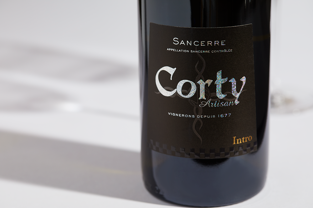 Close up label on a bottle of Moreux Corty Sancerre Blanc Intro 2022 on a white table with shadows of the bottle and 2 wine glasses