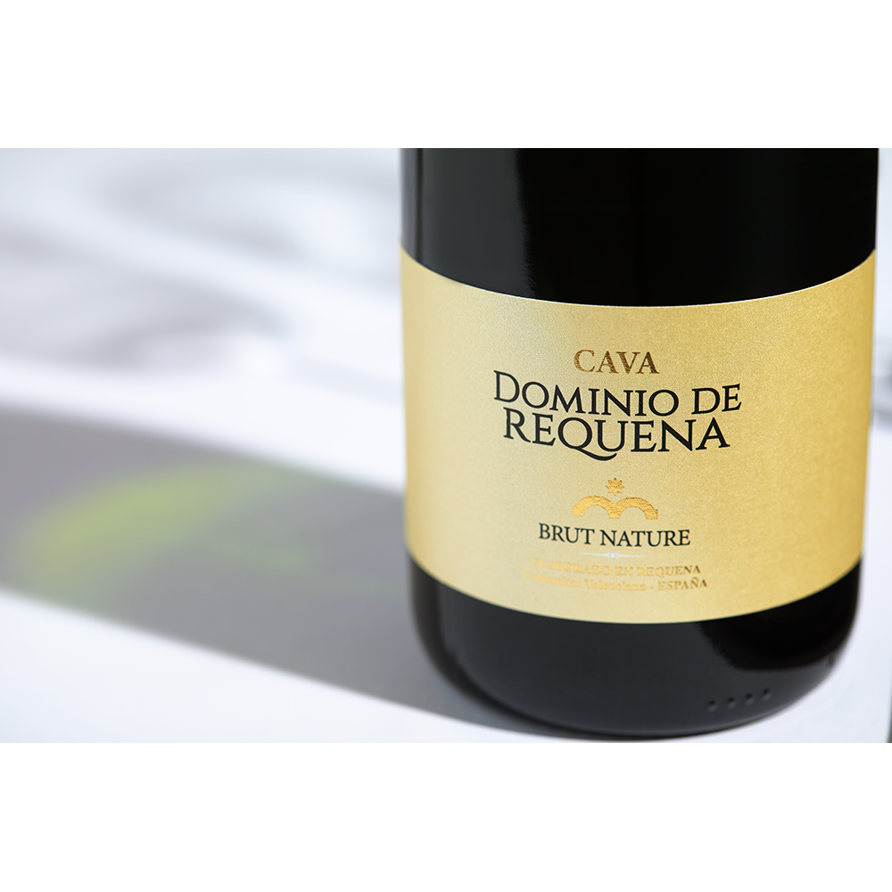 Close up label on a bottle of Pago de Tharsys Dominio Requena Cava Brut Nature Utiel Requena on a white table with shadows of the bottle and 2 champagne glasses