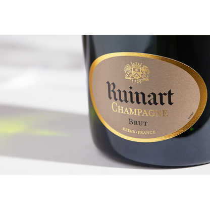 Close up label on a bottle of Ruinart Brut NV on a white table with shadows of the bottle and 2 champagne glasses