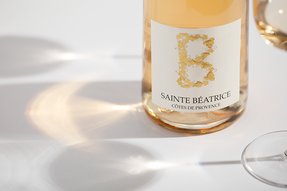 Close up label on a bottle of Sainte Beatrice Cotes de Provence Rosé on a white table with shadows of the bottle and 2 wine glasses