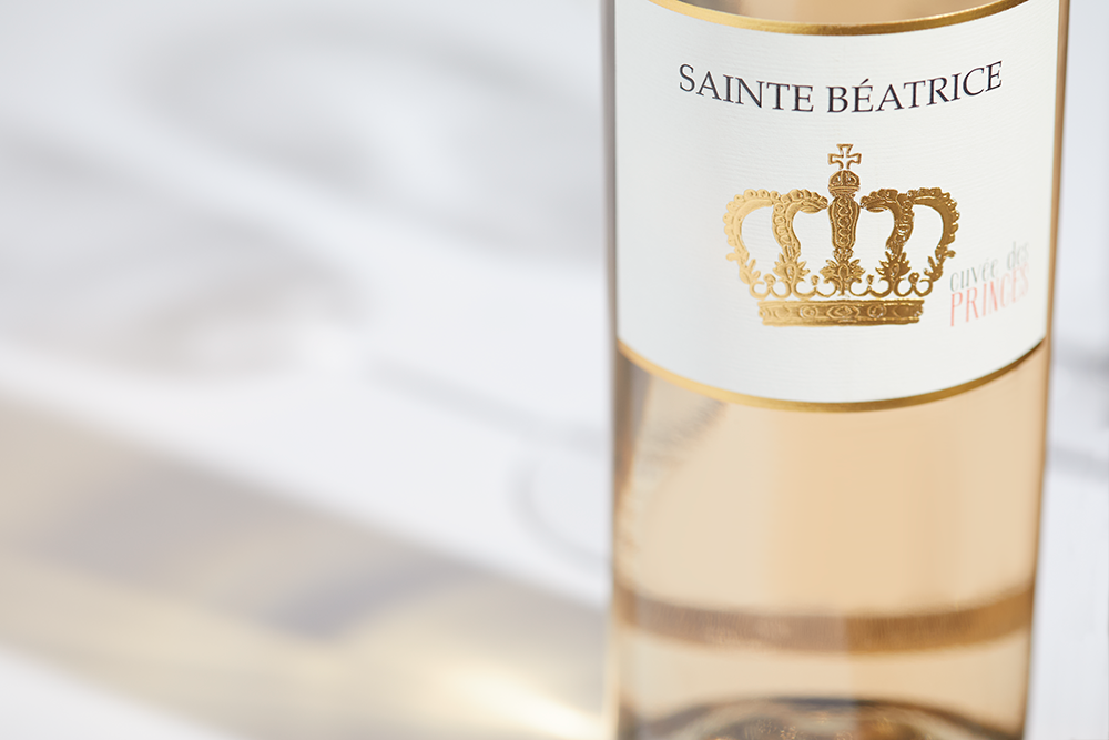 Close up label on a bottle of Sainte Beatrice Cuvee de Princes Rosé on a white table with shadows of the bottle and 2 wine glasses